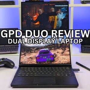 This image shows a dual-display laptop titled "GPD DUO REVIEW." The laptop features two screens, one on top of the other, with the upper screen displaying a scene from a movie or TV show, while the lower screen shows a racing video game. The laptop has a keyboard at the bottom, and there is a game controller and a pen resting on the table next to it. The background shows a shelf with other laptops and tech gadgets. The AMD Ryzen 9 HX processor logo is displayed in the bottom right corner of the image.