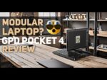 Image featuring a modular laptop, the GPD Pocket 4, on a modern wooden desk in an industrial-style workspace. Text overlay reads 'Modular Laptop? GPD Pocket 4 Review' with an expressive emoji depicting surprise, highlighting the device's unique modular design.