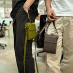 Two individuals wearing AYANEO leather crossbody bags showcasing the green and brown color options The bags are worn comfortably demonstrating their practicality and portability