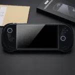 1 A black AYANEO 3 handheld gaming console lies centered on a dark surface, featuring a newly applied tempered glass screen protector. The console's dual joysticks are illuminated with circular white LED rings. To the top right, the product packaging is visible, showing a black box labeled "METIK SCREEN PROTECTOR" with an illustrative diagram of the installation process. The sleek, matte black finish of the device and the glossy reflection on the protected screen create a high-end, tech-focused aesthetic.