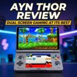 The image features a dual screen clamshell style handheld gaming device centered on a dark surface against a blurred neon lit gaming room background The device is grey with colorful ABXY buttons and glowing blue rings around the joysticks The top screen displays a vibrant 3D Sonic the Hedgehog game while the bottom screen shows a stylized menu or secondary game interfaceThe image features a dual screen clamshell style handheld gaming device centered on a dark surface against a blurred neon lit gaming room background The device is grey with colorful ABXY buttons and glowing blue rings around the joysticks The top screen displays a vibrant 3D Sonic the Hedgehog game while the bottom screen shows a stylized menu or secondary game interface