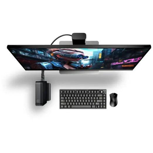 GPD BOX mini PC mounted beneath an ultrawide monitor, black ribbed case with keyboard, mouse, and webcam